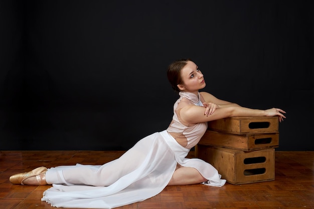 Foto ballerina in een witte jurk en pointe schoenen zit op de vloer op een zwarte achtergrond