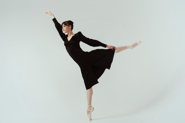 Ballerina in een zwarte jurk en pointes poseert in een fotostudio in beweging met mooie lange benen