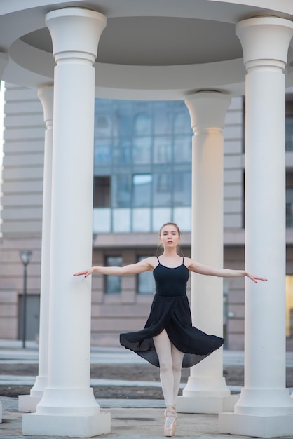 Ballerina in een zwarte jurk is een mooie pose Een mooie jonge vrouw in een zwarte bodysuit danst in een elegante klassieke dans op een achtergrond van kolommen