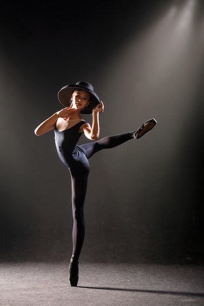 Ballerina in nauwsluitend pak danst op zwarte achtergrond op pointe-schoenen, silhouet wordt verlicht door kleurbronnen.