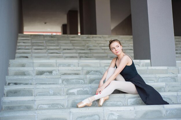 Ballerina in tutu poseren zittend op de trap Een mooie jonge vrouw in een zwarte jurk en spitzen rust zittend in een elegante pose op de trap van buitenaf