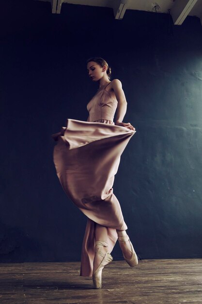 Photo ballerina in a pink dress and punts moves around the room with a fluttering dress