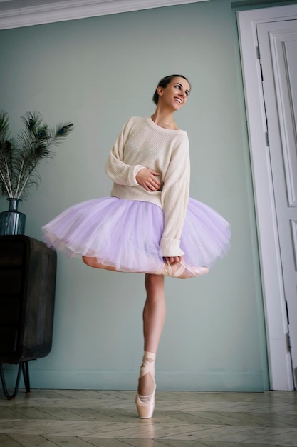 Ballerina poseert met haar benen in de kamer voor de spiegel in pointe-schoenen en tutu