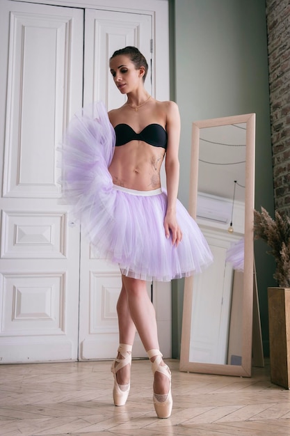 Ballerina poseert met haar benen in de kamer voor de spiegel in pointe-schoenen en tutu