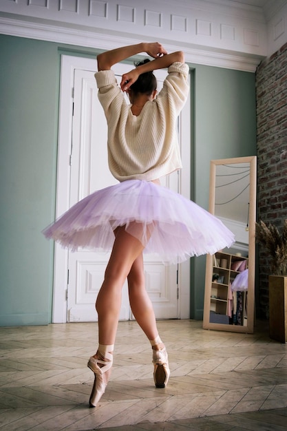 Ballerina poses showing her legs in the room in front of the\
mirror in pointe shoes and tutu