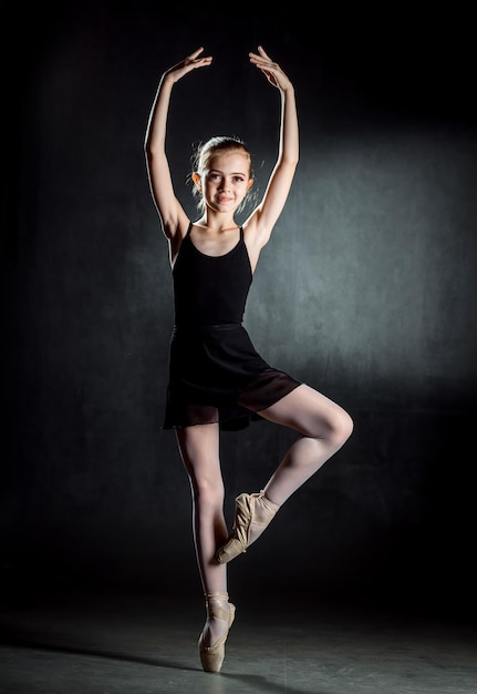 Ballerina Schattig klein meisje poseren en dansen op het podium Het meisje studeert ballet Donkere achtergrond