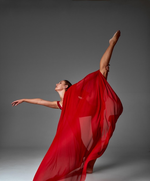 Ballerina springen in Pointe-schoenen met vliegende rode doek moderne balletdans geïsoleerd grijze achtergrond