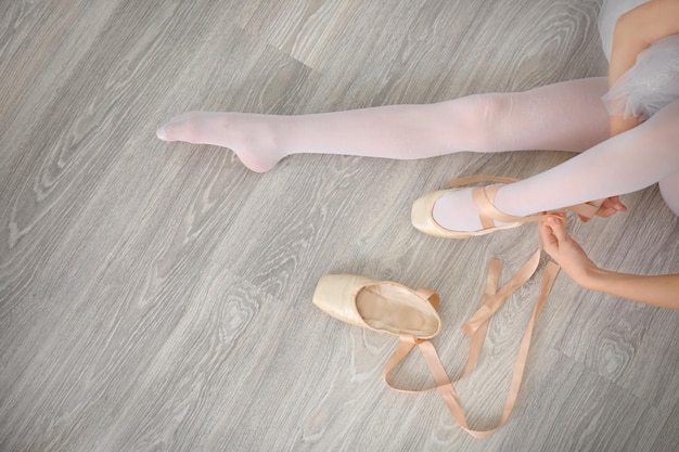 Photo ballerina tying ballet shoes on wooden floor