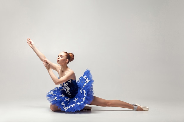 Ballerina wearing blue dress and pointe shoes graceful sitting on white studio floor