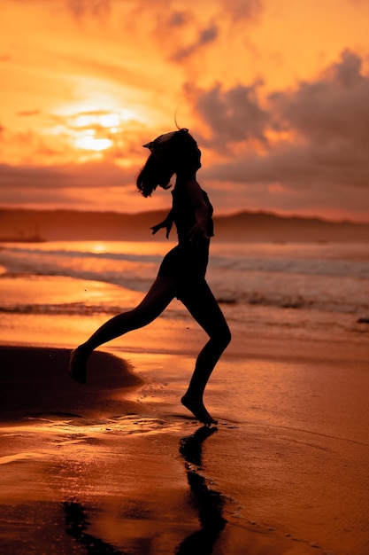 A ballerina with a silhouette shape performs ballet movements very flexibly on the beach with the waves crashing