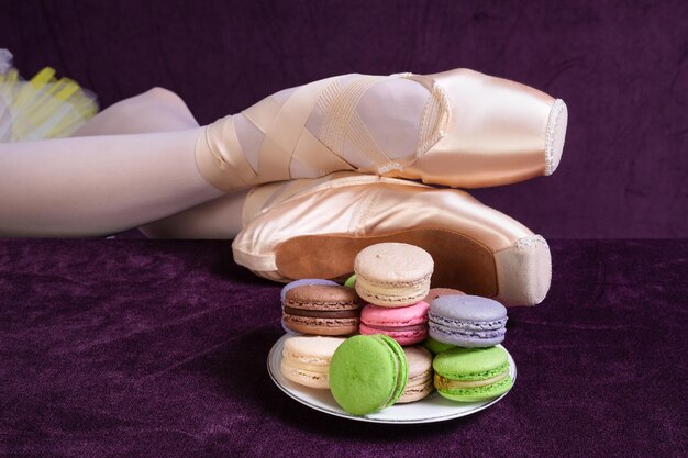 Ballerinas legs in pointe shoes and bright sweets macaron cake