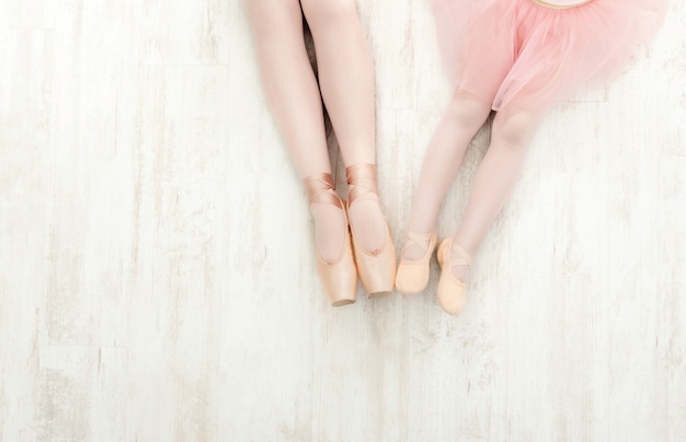 Foto sfondo di balletto. bambina e giovane ballerina gambe in scarpe da punta su pavimento in legno bianco, vista dall'alto con spazio copia. sfondo della scuola di danza classica, pratica per i bambini