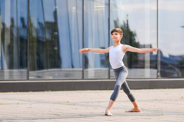 Балетный мальчик-подросток танцует на фоне отражения города и неба в стеклянной стене