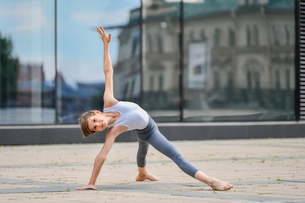 Ballet boy teenager trains standing on his hands against the background of the reflection of the city and sky in the glass wall