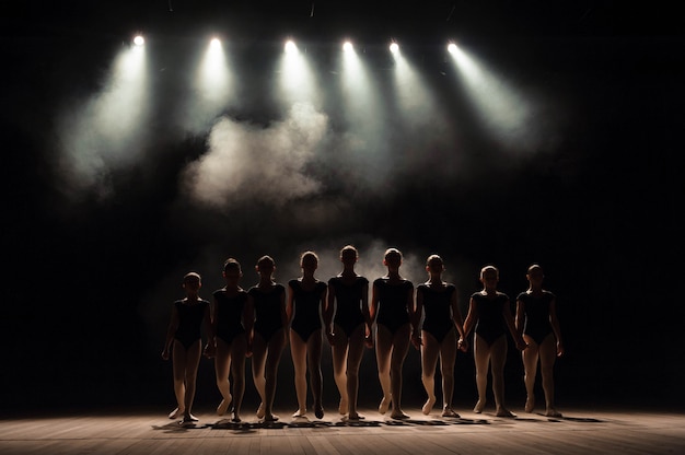 Ballet class on the stage of the theater with light and smoke. Children are engaged in classical exercise on stage.