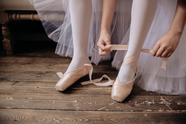 Ballet dancer's feet on studio floor. Teenage dancer puts on ballet pointe shoes copyspace.