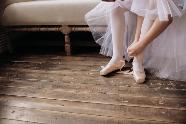 Ballet dancer's feet on studio floor. Teenage dancer puts on ballet pointe shoes copyspace.