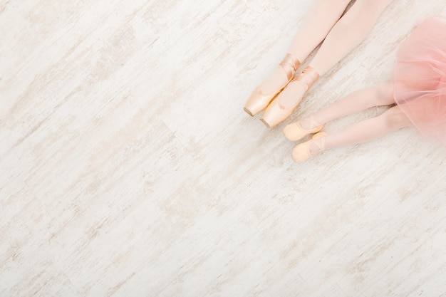 Balletachtergrond. Klein meisje en jonge ballerina benen in pointe-schoenen op witte houten vloer, bovenaanzicht van bovenaf met kopieerruimte. Klassieke dansschoolachtergrond, oefenen voor kinderen