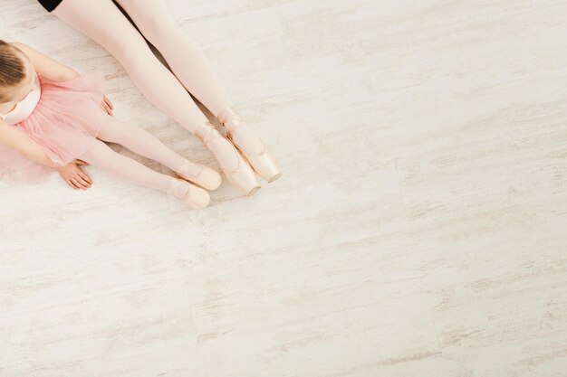 Balletachtergrond. Klein meisje en jonge ballerina benen in pointe-schoenen op witte houten vloer, bovenaanzicht van bovenaf met kopieerruimte. Klassieke dansschoolachtergrond, oefenen voor kinderen