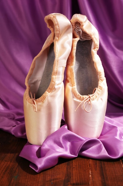 Balletpointe-schoenen op houten vloer op stoffenachtergrond