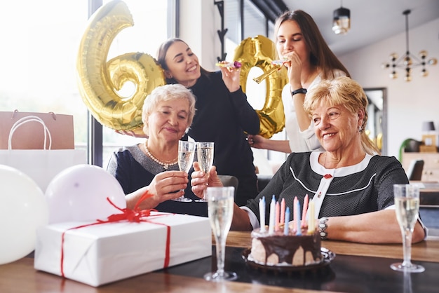 Ballonnen met nummer 60. Senior vrouw met familie en vrienden die een verjaardag binnenshuis vieren.