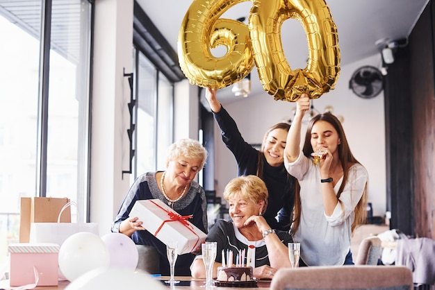 Ballonnen met nummer 60. Senior vrouw met familie en vrienden die een verjaardag binnenshuis vieren.