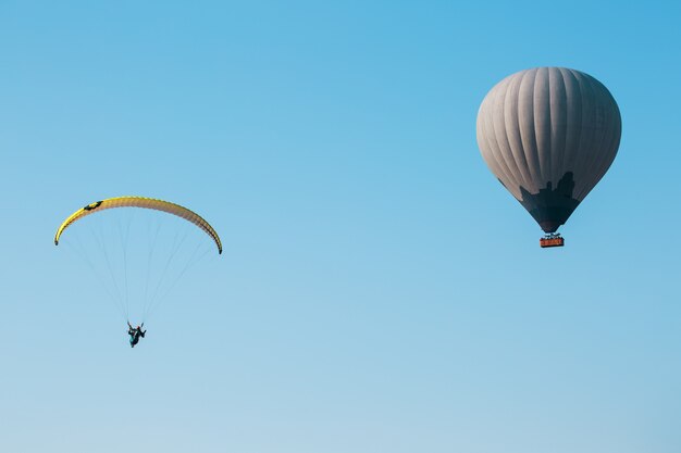 Balloon and paraglider soars against the blue sky