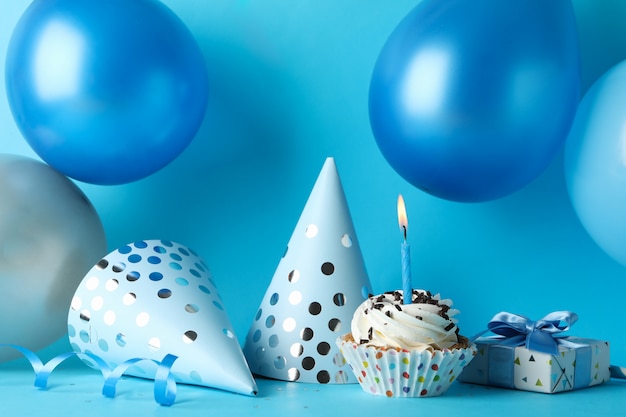 Balloons, birthday hats, cupcake and gift box on blue background, close up