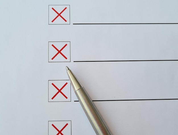 Фото Шариковая ручка вычеркивает элементы контрольного списка красным крестиком на белой бумаге.