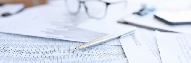 Ballpoint pen and glasses lying on documents with numbers closeup