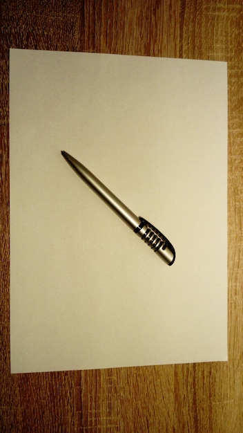 A ballpoint pen lies on a white sheet of paper Paper and pen lies on a wooden table