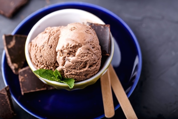 チョコレート、ミント、木の棒が付いている青い受け皿のボウルのチョコレート溶けるアイスクリームのボール
