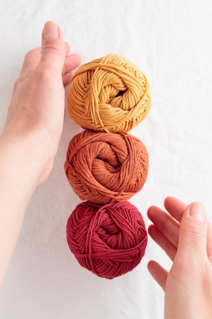 Balls of cotton yarn warm colors on a white table with hands