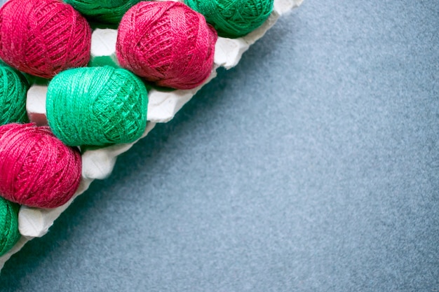 Фото Шары цветной красной и зеленой пряжи в лотке для бумажных яиц