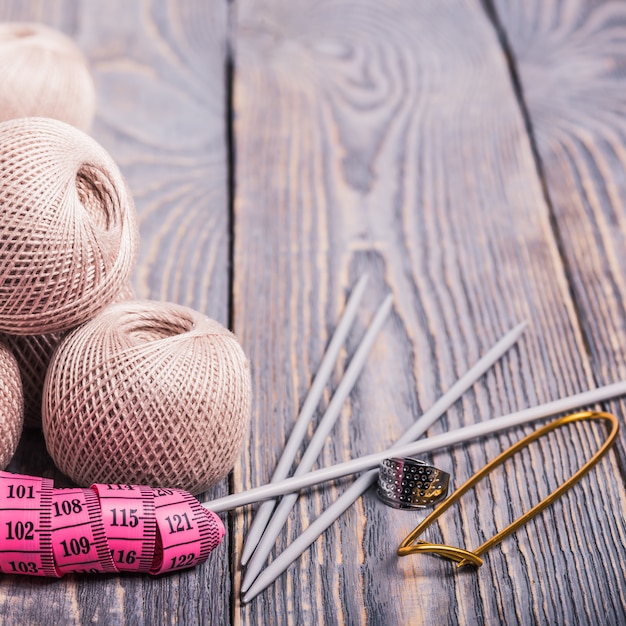 Balls of yarn, knitting needles and measuring tape on a wooden background.