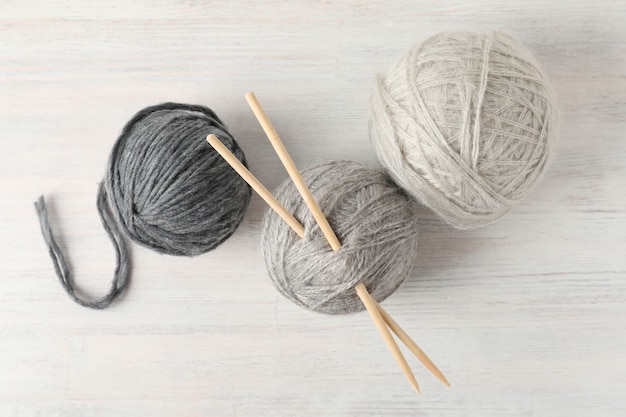 Balls of yarn with knitting needles on white wooden background.