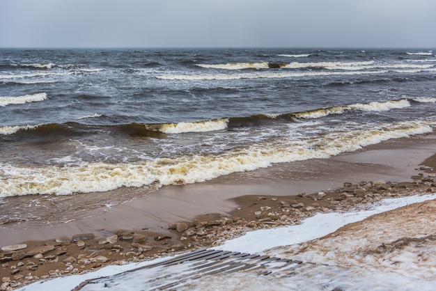 Фото Пляж балтийского моря зимой снежный, а в море большие волны. пешеходная дорожка между зимними дюнами балтийского моря в саулкрасты в латвии