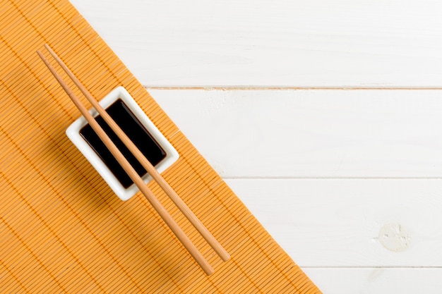 Bamboe mat en sojasaus met sushi stokjes op witte houten tafel. Bovenaanzicht met kopie ruimte achtergrond voor sushi. plat leggen