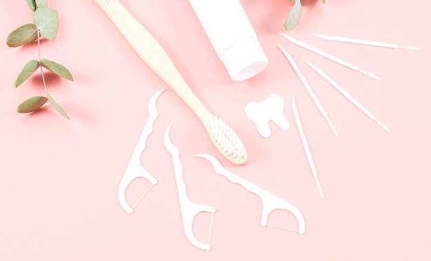Bamboe tandenborstel tandzijde tandenstokers een tube tandpasta en een papieren tand op een zachtroze