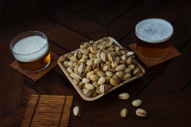 Bamboo bowl plenty of pistachios and two glasses of beer in a pub. Wooden table. Summer party celebration.