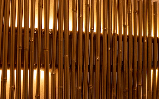 Bamboo branches painted in golden colors with backlight. Wall decoration, lamp. Full frame close-up photo. Illuminated bamboo trunks in the interior. Space for text. Abstract background and texture.