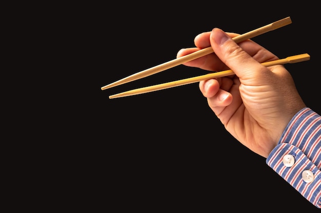 Photo bamboo chopsticks in a male hand on a dark background items for food