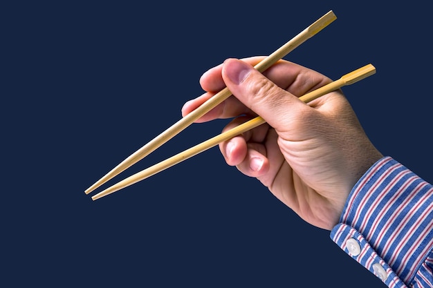 Bamboo chopsticks in a male hand on a dark background items for food