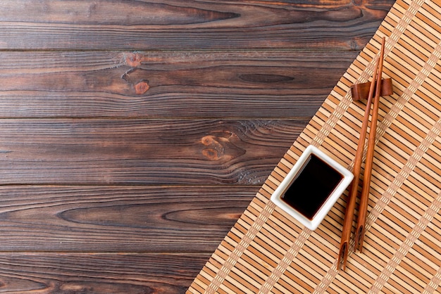 Bamboo mat and soy sauce with sushi chopsticks on wooden table Top view with copy space background for sushi Flat lay