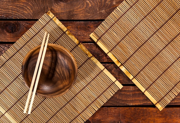 Bamboo mat on wooden table with bowl and chopsticks