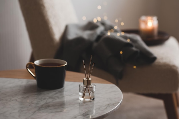 Bamboo sticks in bottle with scented candles and cup of tea on marble table closeup Home aroma Aromatherapy Apartment living