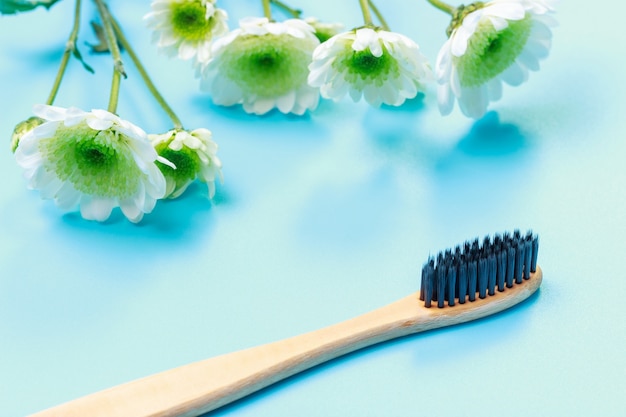 Spazzolino da denti in bambù e fiori su sfondo blu da vicino.