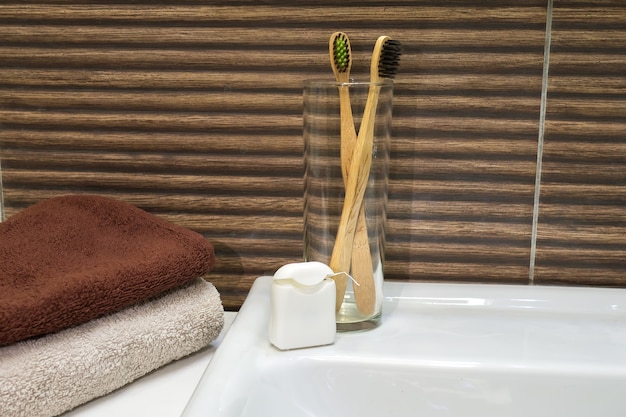 Photo bamboo toothbrush in glass stand with towel and dental floss in zero waste bathroom