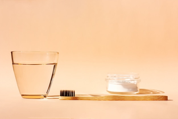 竹の歯ブラシ、コップ一杯の水、オレンジの歯磨き粉