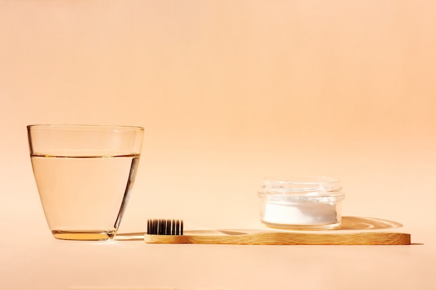 Bamboo toothbrush, glass of water and toothpaste powder on orange